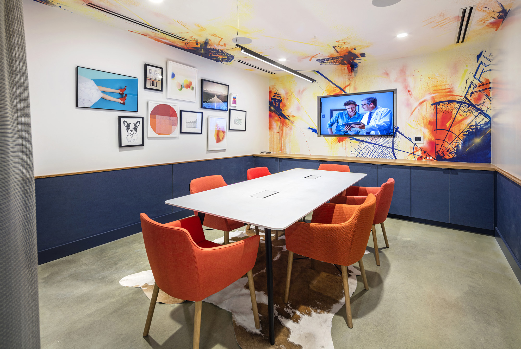 a conference room with a white table and orange chairs and a tv on the wall